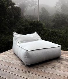 a white bean bag sitting on top of a wooden deck next to trees in the fog