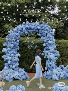 a woman walking past a blue flower arch