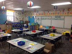 a classroom filled with lots of desks covered in papers and balloons hanging from the ceiling