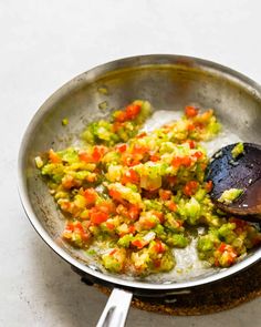 a pan filled with vegetables on top of a white counter next to a wooden spoon