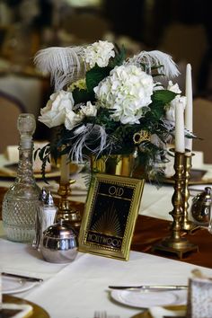 there is a vase with white flowers and feathers on the table at this wedding reception