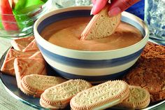 a person dipping crackers into a bowl of peanut butter dip with cookies on the side