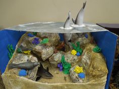 two white birds sitting on top of rocks in a box with water and seaweed