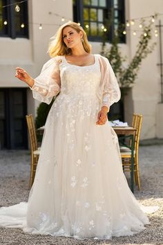 a woman in a white wedding dress standing on the ground with her arms out and looking at the camera