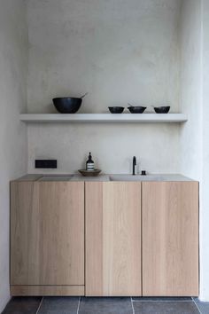 a kitchen with wooden cabinets and black bowls on the counter top in front of a white wall