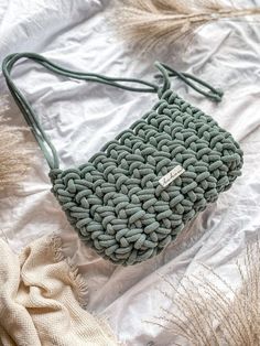 a knitted purse sitting on top of a white cloth covered bed next to dried grass