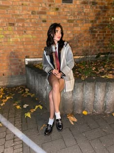 a woman sitting on a bench in front of a brick wall with her legs crossed