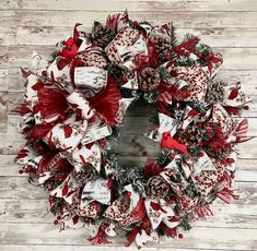 a red and white christmas wreath hanging on a wooden wall with pine cones, bows and other holiday decorations