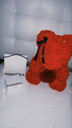 a red teddy bear sitting on top of a bed next to a box with a black ribbon