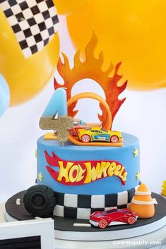 a birthday cake with hot wheels on top and balloons in the air behind it that say 4 o'clock