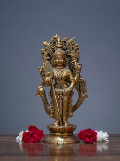 a golden statue sitting on top of a wooden table next to red and white flowers