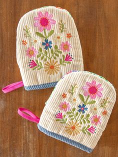 two oven mitts with flowers on them sitting on a wooden table next to a pink ribbon