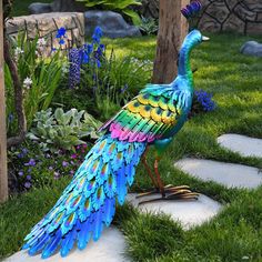 a colorful peacock statue sitting on top of a lush green field next to a stone walkway