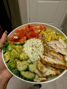 a person holding a bowl filled with chicken, vegetables and dressing