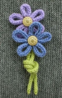 a crocheted flower on top of a gray sweater with green and blue yarn