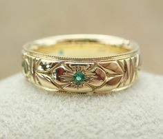 a gold wedding band with an emerald stone in the center, on a white surface