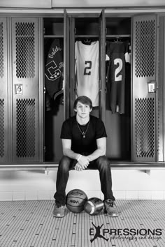 a man sitting on a bench in front of lockers with basketballs and jerseys