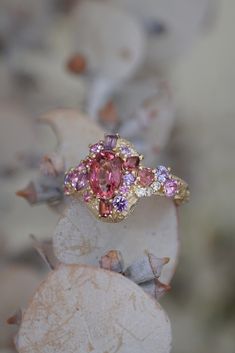 a pink and yellow diamond ring sitting on top of a leafy plant with leaves in the background