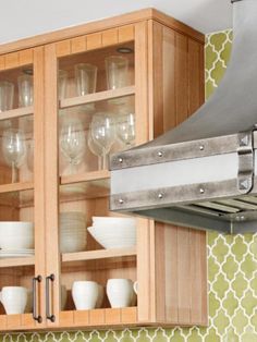 a kitchen cabinet filled with dishes and wine glasses on it's shelf next to a stove