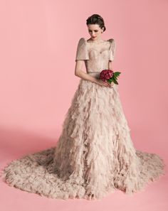 a woman in a white dress holding a bouquet of flowers and standing on a pink background