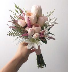 a hand holding a bouquet of flowers on a white background with pink and white blooms