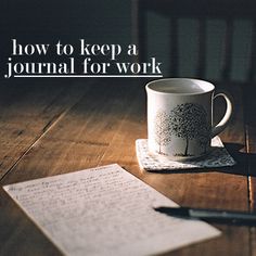 a coffee cup sitting on top of a wooden table next to an open book and pen