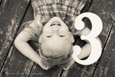 a young boy holding the number three in front of his face while standing on a wooden deck