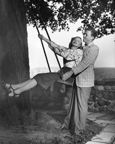 an old photo of a man and woman swinging on a tree swing in the 1950's