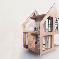 a doll house made out of wood with windows and stairs to the second floor, sitting on a white surface