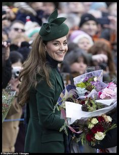 a woman in a green coat and hat holding flowers