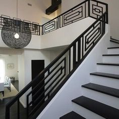 a staircase with black and white railings in a modern style home, looking down at the living room