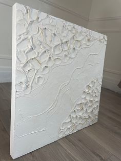 a large white piece of art sitting on top of a hard wood floor next to a wall