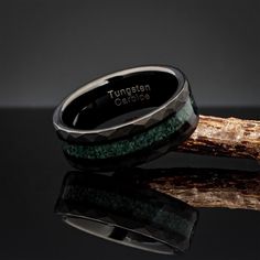 a black and green ring sitting on top of a piece of wood with the words tunsten