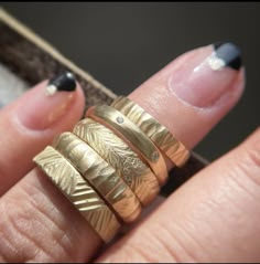 a woman's hand with three gold rings on her fingers and two black nails