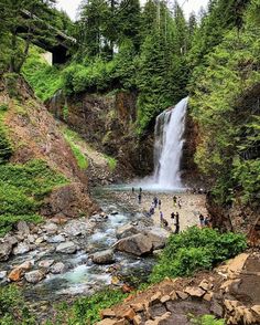 people are standing at the base of a waterfall