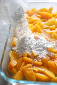 a glass baking dish filled with powdered sugar and peaches, on top of a table