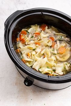 a crock pot filled with chicken noodle soup on a white counter top next to a spoon