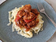 a blue plate topped with pasta and meat covered in tomato sauce next to a fork