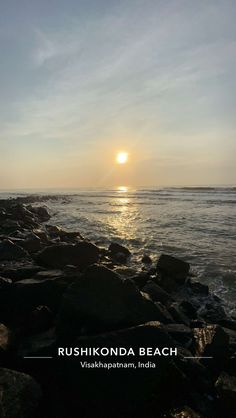 the sun is setting over the ocean with rocks on the shore and water in the foreground