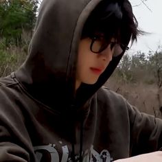 a young man wearing glasses and a hoodie looking at his cell phone in the woods