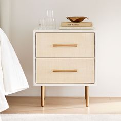 a white nightstand with two drawers on top of it and a book next to it