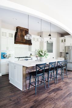 a large kitchen with white cabinets and wooden flooring is seen from across the room