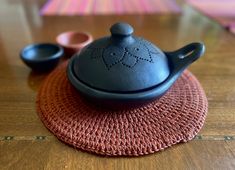 a black teapot sitting on top of a red place mat