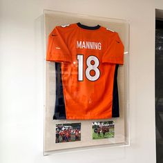 an orange jersey hanging on the wall in front of a glass display case with photos