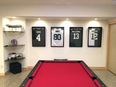 a pool table in a room with three jerseys on the wall