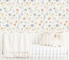 a baby crib with a floral wallpaper in the corner and a white crib bed next to it