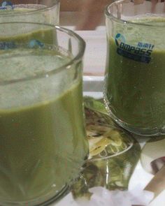 two glasses filled with green liquid sitting on top of a table