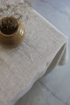 a small gold vase sitting on top of a white table cloth covered table with dried plants in it