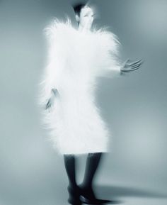 a woman in a white fur coat and black boots is standing with her arms outstretched