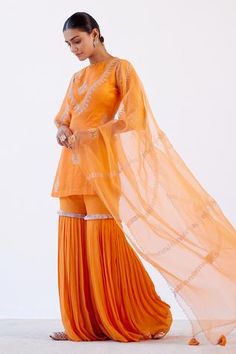 Orange kurta with dori and sequins embroidery. Paired with a pleated sharara detailed with rose gold lace and embroidered organza dupatta. 
Component: 3
Pattern: Embroidered
Type Of Work: Dori,Sequins
Neckline: Round
Sleeve Type: Long Sleeves
Fabric: Linen Satin and Organza
Color: Orange
Other Details: 
Embroidered dupatta
Back cutout kurta
Scallop sharara
Occasion: Wedding - Aza Fashions Orange Sharara, Satin Kurta, Wedding Outfits Indian, Dori Embroidery, Rose Gold Lace, Embroidered Sharara, Kurta Sharara Set, Kurta Sharara, Outfits Indian